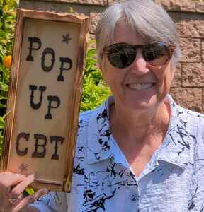 Christine Padesky wearing sunglasses and holding a sign that reads Pop Up CBT